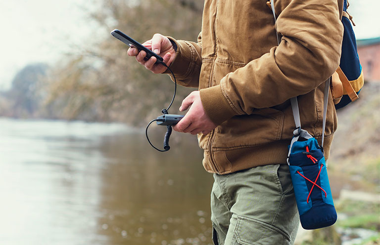 man holding cell phone with portable charger, he has a water bottle attached to his clothes by a string