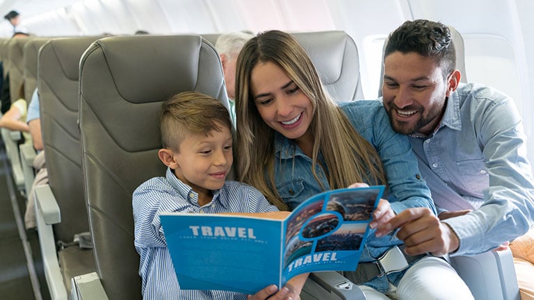 Portrait of a happy family traveling by plane and reading a travel guide - lifestyle concepts; Credit: Hispanolistic