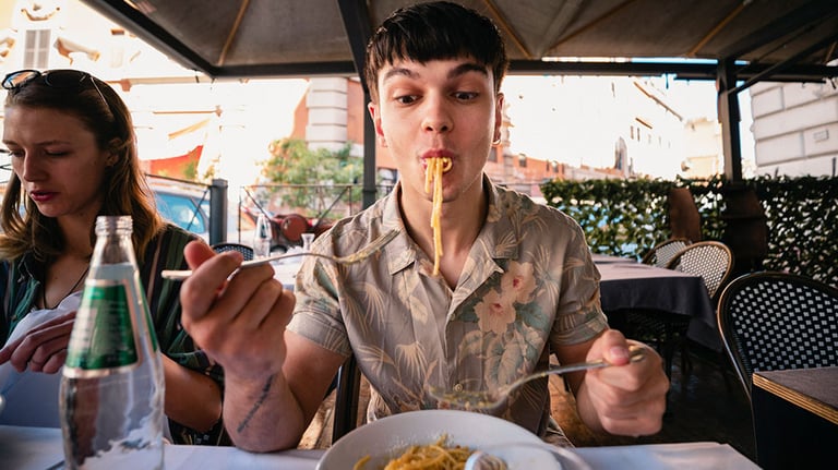 A front-view shot of a young man enjoying a delicious meal in Italy, he is wearing casual clothing. Credit: SolStock