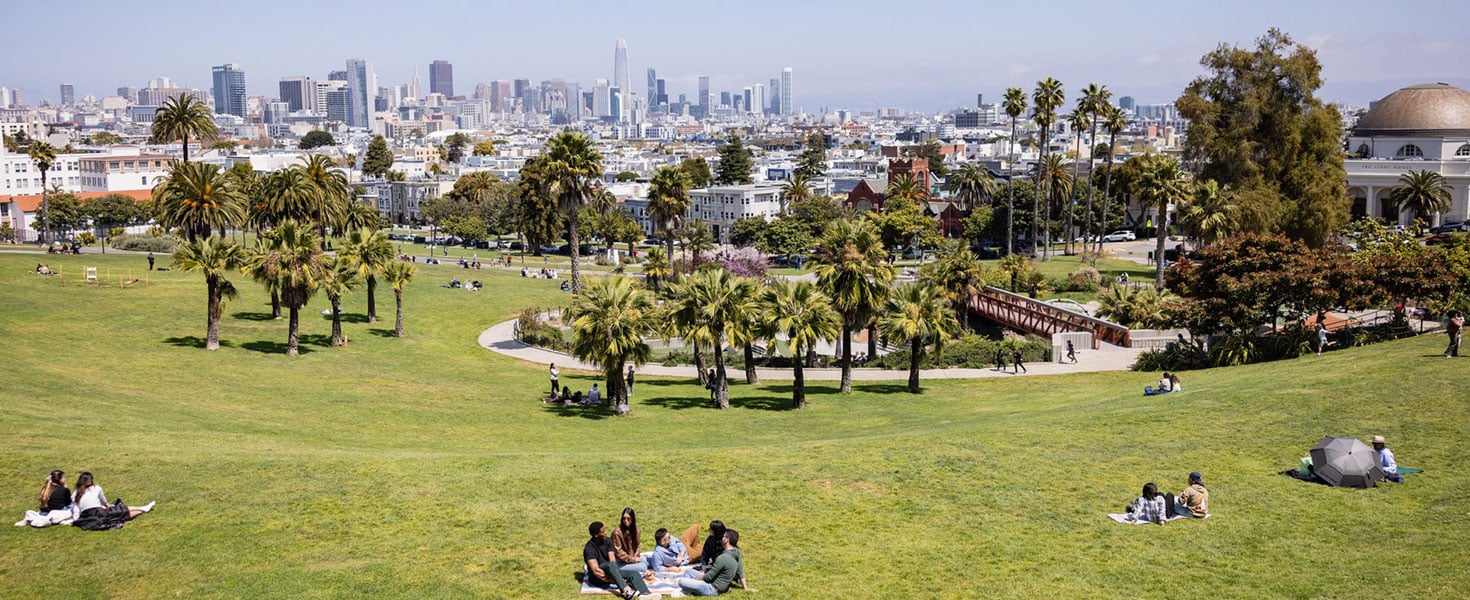 Picnickers scattered across sunlit Dolores Park with the San Francisco skyline rising in the distance; photo courtesy of San Francisco Travel