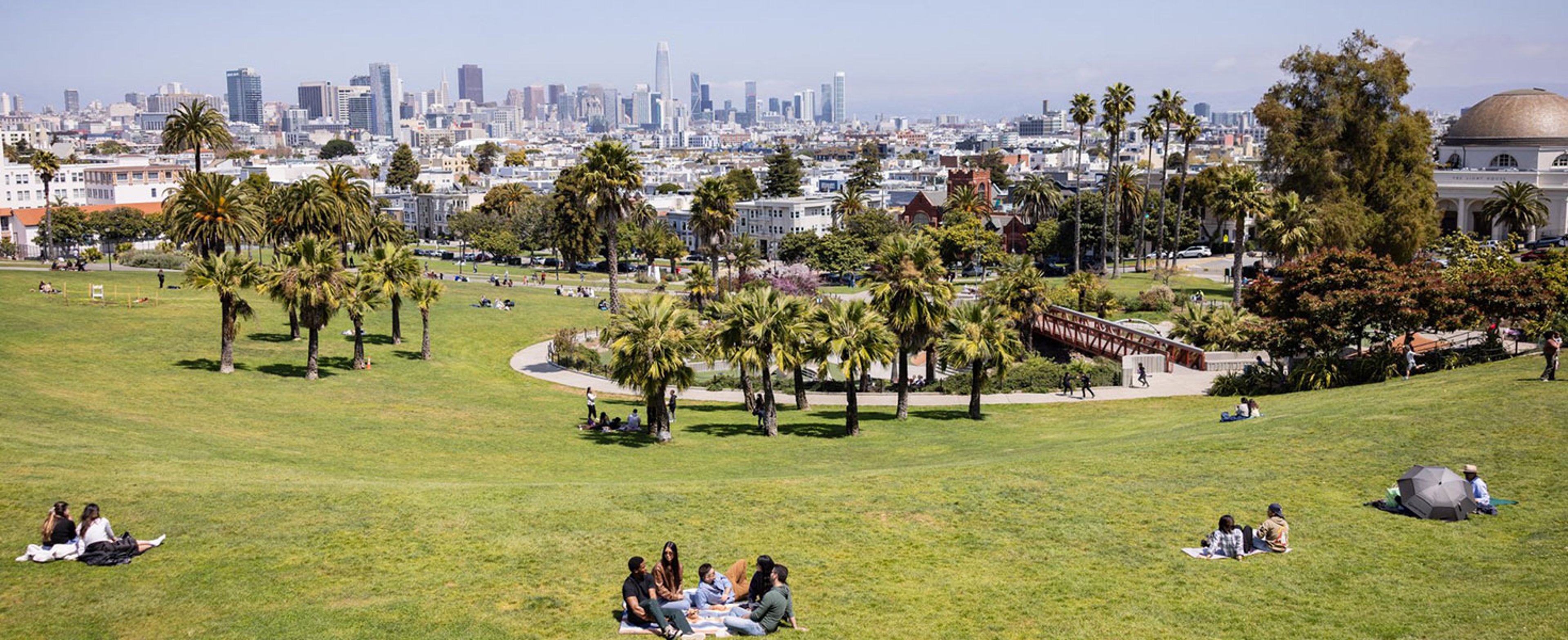 Picnickers scattered across sunlit Dolores Park with the San Francisco skyline rising in the distance; photo courtesy of San Francisco Travel