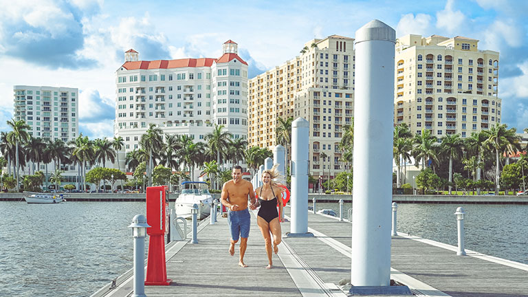 Beautiful adventurous couple run down a dock in swimwear holding hands; Credit:Lisa5201
