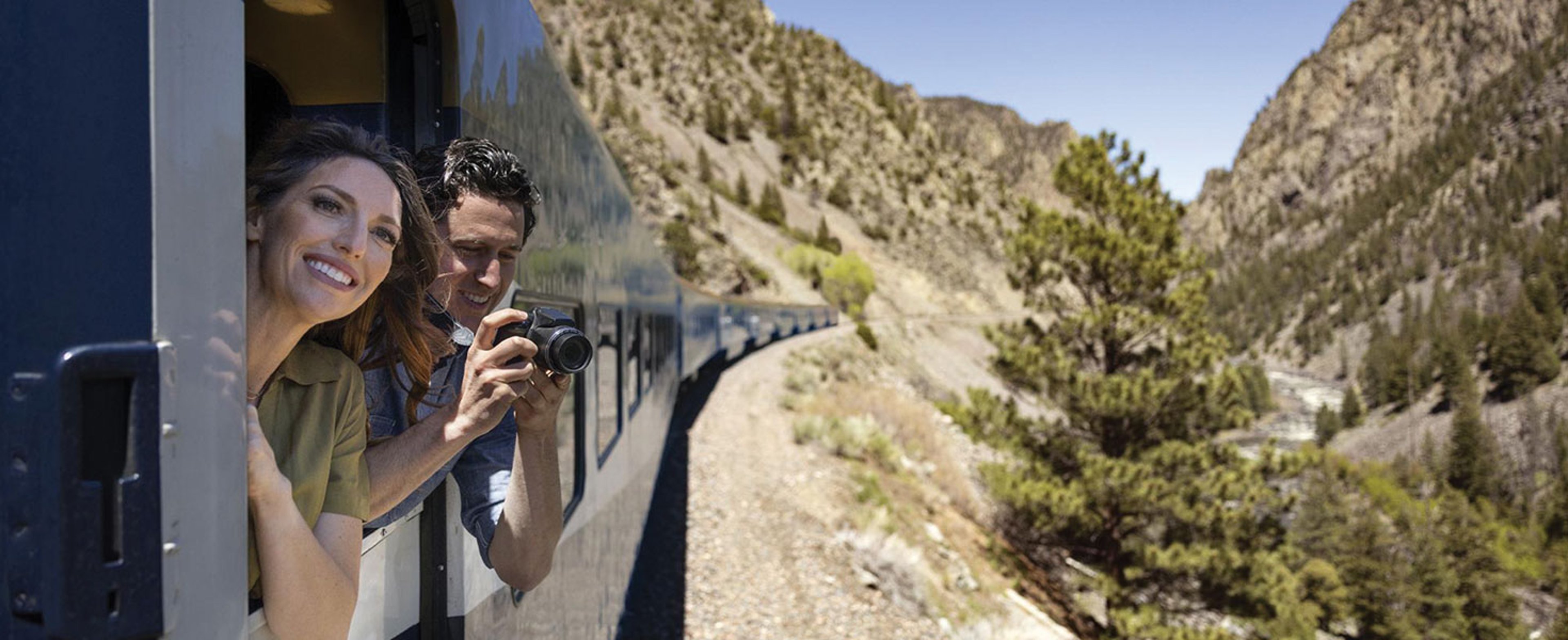 Couple leaning out of a train window through a mountain canyon; photo courtesy of Rocky Mountaineer.