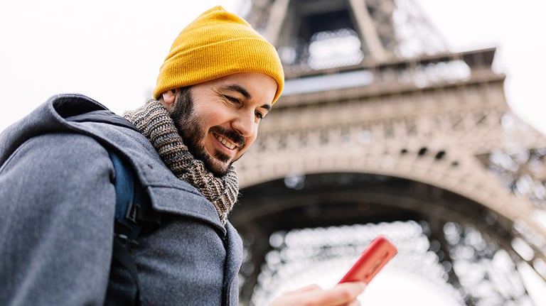 Happy young adult tourist man using mobile phone close to Eiffel Tower in Paris. Communication and travel concept.  by Xavier Lorenzo