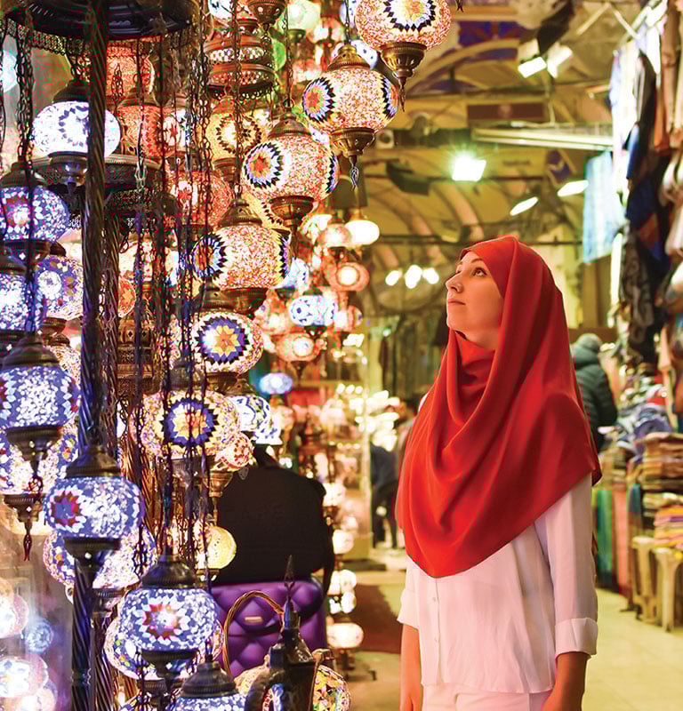Young pretty tourist Muslim woman with red scarf looking on Traditional Turkish lamps in souvenir shop. Woman in hijab shopping in the Grand Bazar. Shopping tour; by Ersin