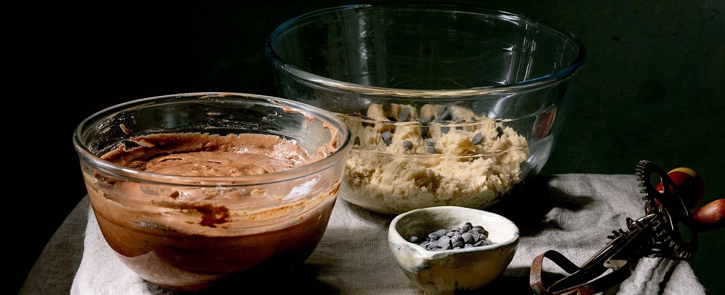 Tow types of dough chocolate and shortbread for home baking trend dessert brookies brownies and cookies in glass bowls, with chocolate chips and vintage hand mixer on linen table cloth.