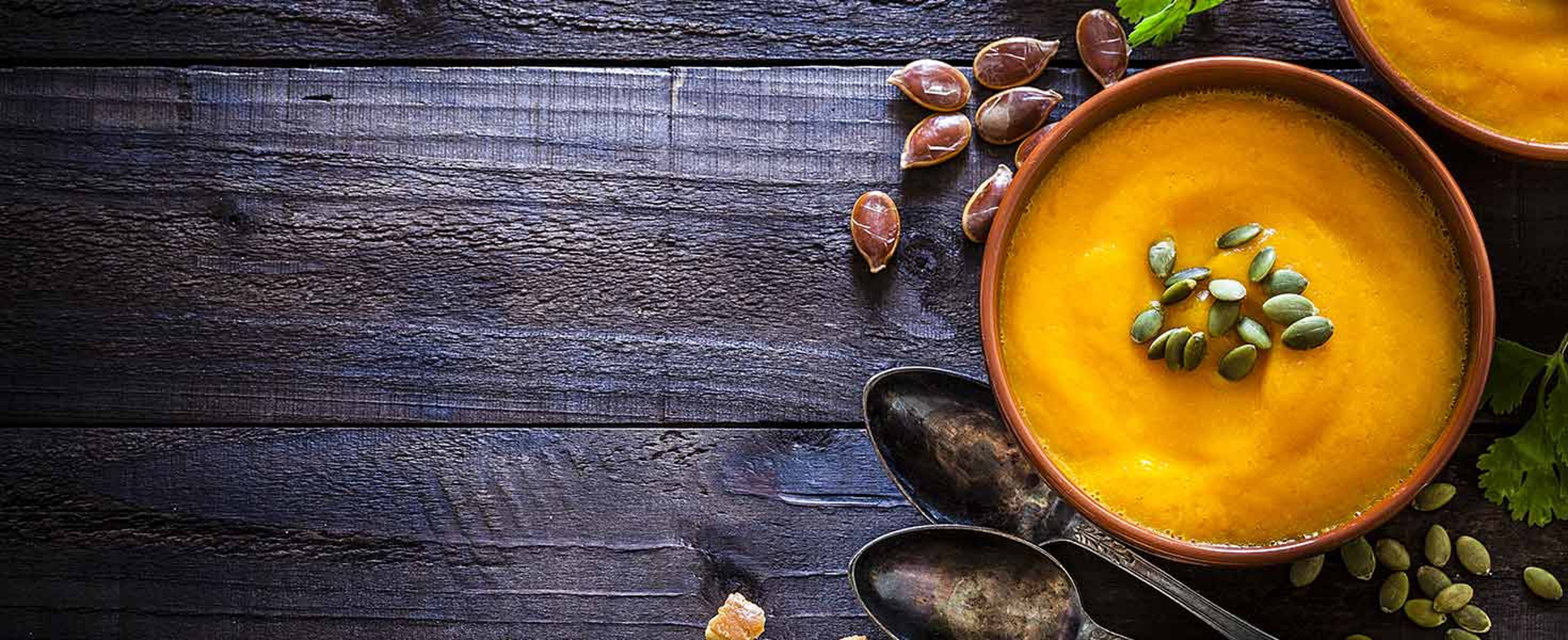 Two brown bowls filled with homemade pumpkin soup surrounded by ingredients