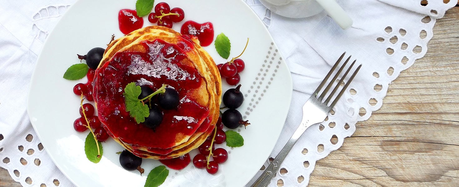 Stack of delicious pancakes with berries and jam on white background.