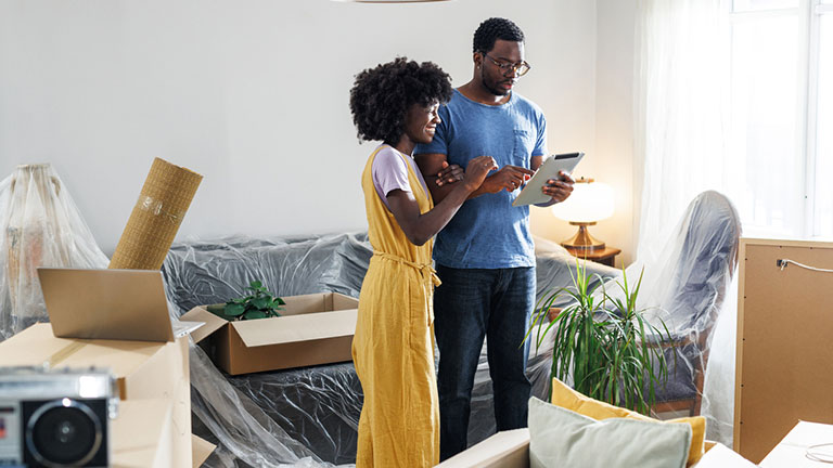 Young African American couple using tablet in their new home, surrounded with unpacked boxes