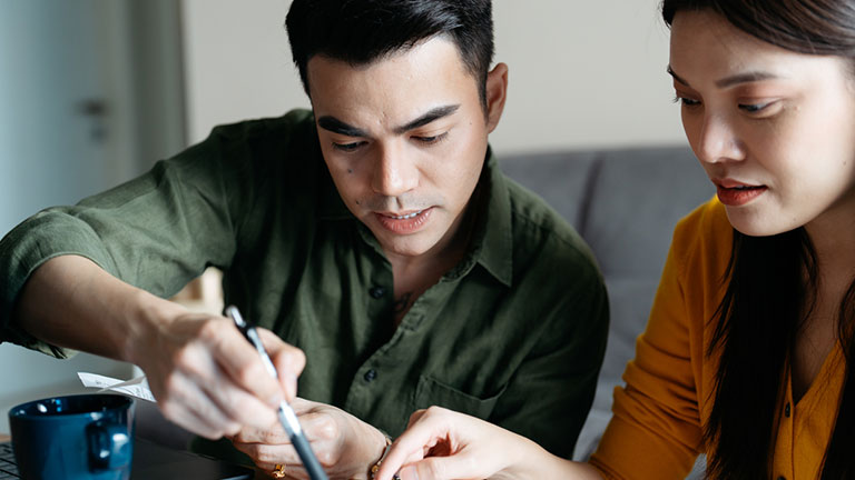 Asian couple managing household budget, planning investment, analyzing paper utility bills, making payments and fill application forms together