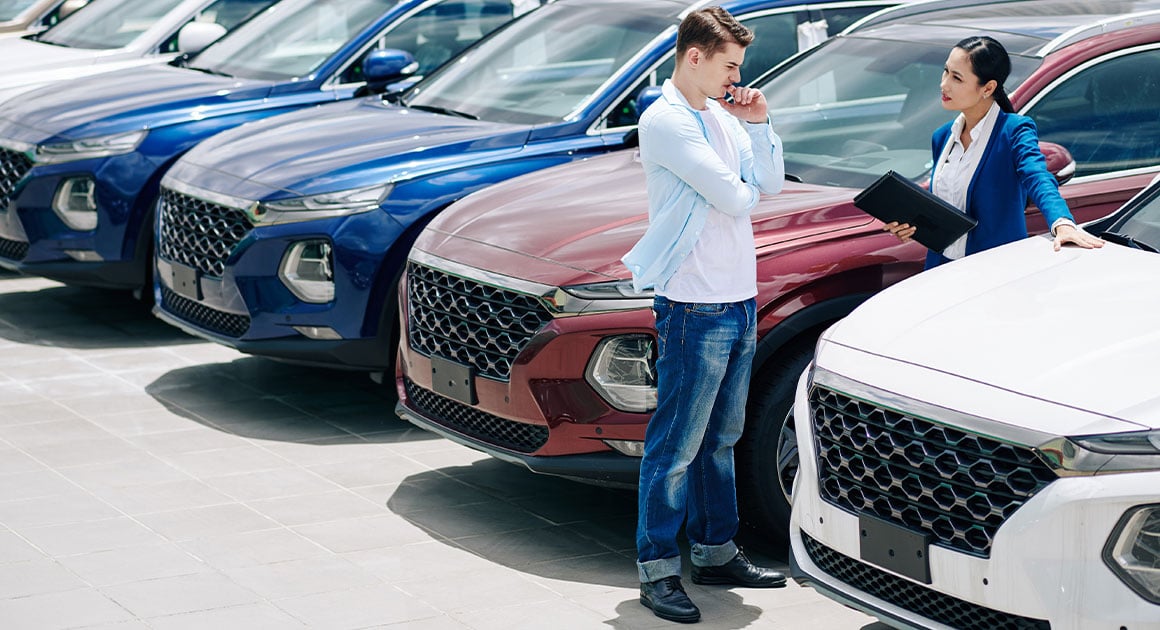 man talking to woman in parking lot of car dealership