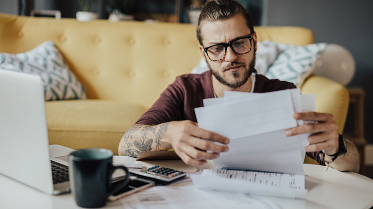 Two Caucasian females doing finances at home together. Cute brunette female sittign at desk with her blonde mother helping her to manage utility bills, surrounded with papers, having focused looks; by shurkin_son
