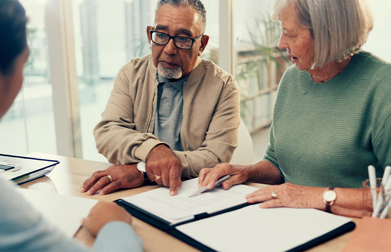 elder couple looking at documents and pointing at them while talking to worker behind desk