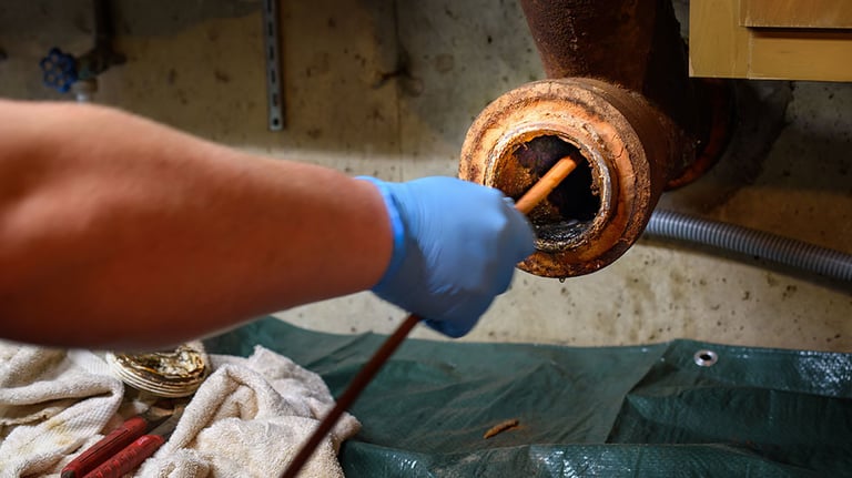 Hands of a plumber as he runs a camera scope and cleaning machine through the main pipe to unclog the drain to the Septic System. Hard-working tradesman; by Chet Wiker