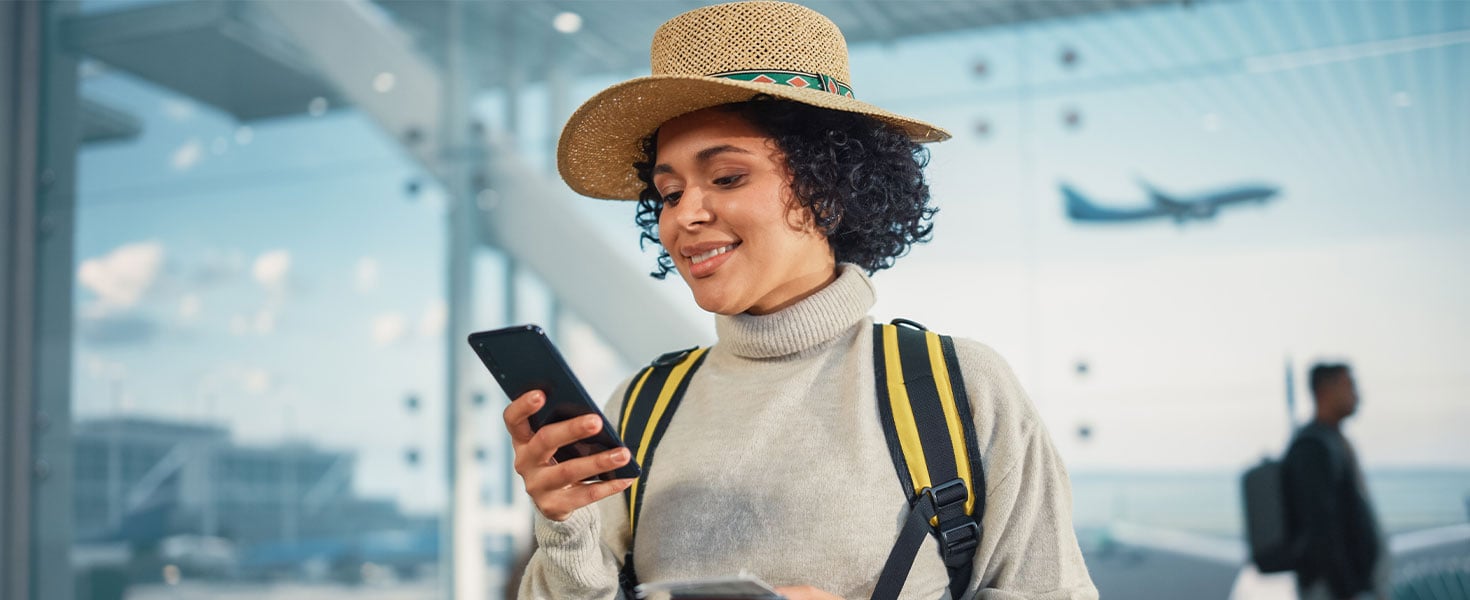 woman using phone at airport, plane seen taking off behind her