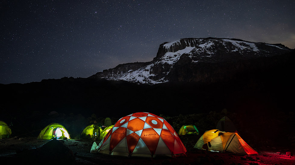 Lighted tents in the night in front of Mount Kilimanjaro