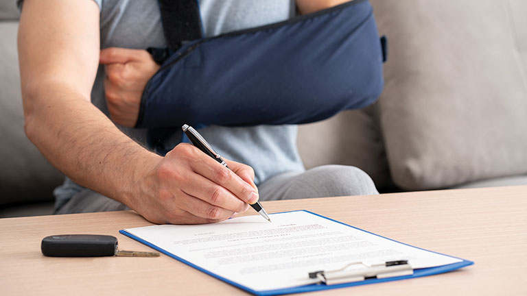 Close up of a man hands with broken arm signing insurance document after car accident at home  by cunaplus