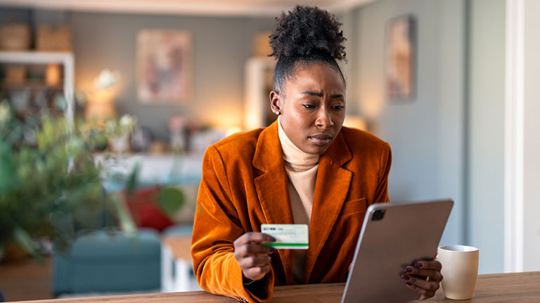 Worried young adult woman holding credit card while checking electronic bank account over digital tablet pc.