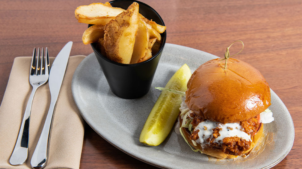 Chicken sandwich on plate with fries and pickle made by Chef Partner Brandon Whitestone of Theismann’s Restaurant