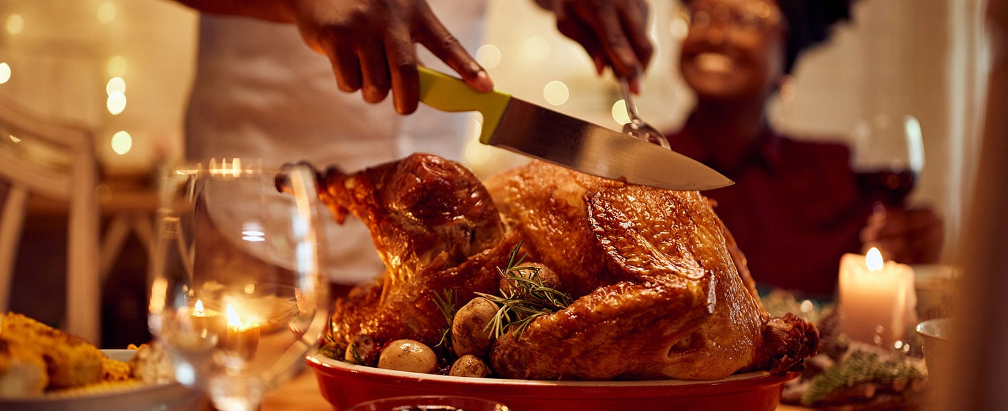 Close-up of black man carving roasted turkey during Thanksgiving meal at dining table. Credit: Drazen Zigic