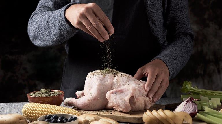 closeup of a young caucasian man preparing a turkey placed on a rustic wooden table full of ingredients to stuff it such as apple, onion or different spices, and celery or a roast corn on the cob. Credit: nito100