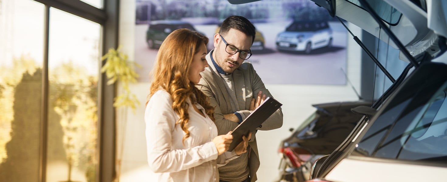 Saleperson reviewing papers with customer in front of car