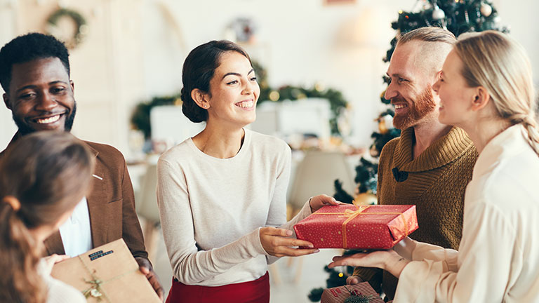 Group of elegant young people exchanging gifts and smiling cheerfully during Christmas party, copy space By Seventyfour