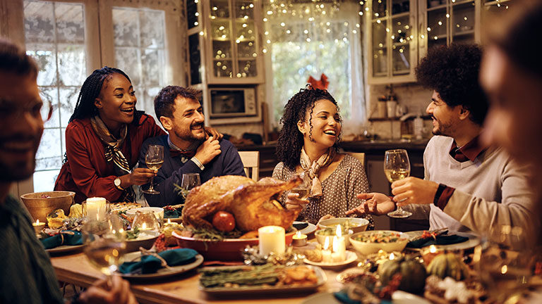 Multiracial group of friends have fun while talking during Thanksgiving dinner at dining table. By Drazen