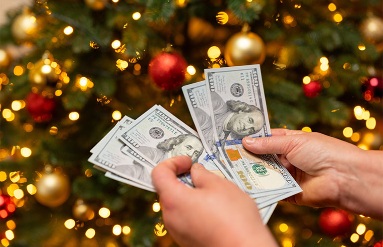 person counting money in front of christmas tree
