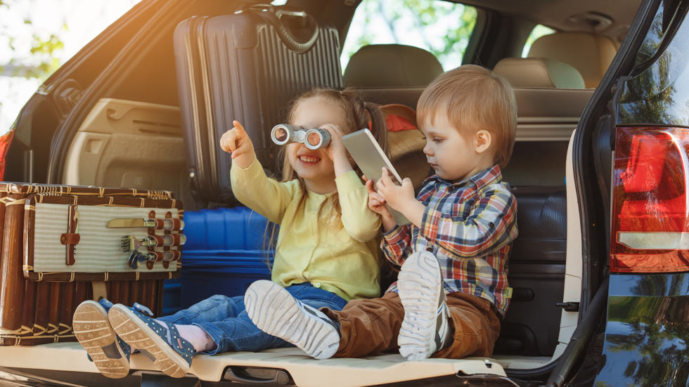 Boy & Girl Toddlers in the back of the trunk of car with vacation items.