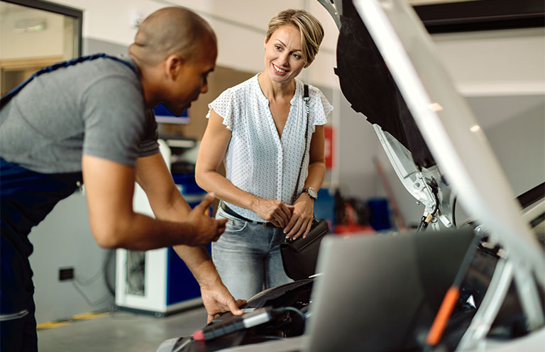 Happy woman talking to her car mechanic in a repair shop