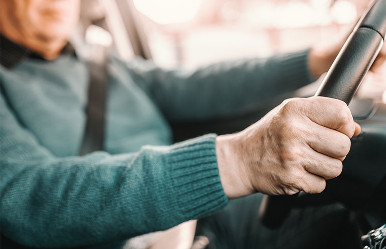 elder man with hands on steering wheel driving