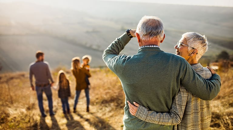 Back view of embraced grandparents enjoying while looking at their family on a hill in autumn day. Credit:skynesher