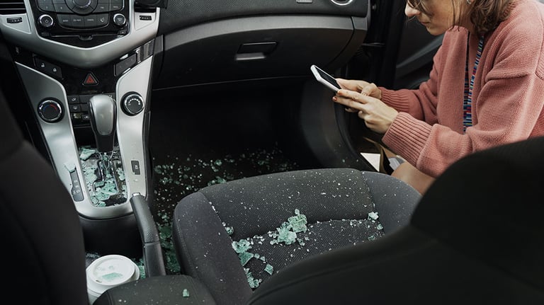 Young woman taking photos using a smart phone of the inside of her car covered in broken window glass after a break in Credit:AJ_Watt