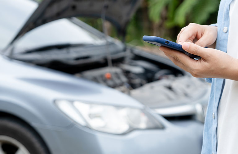 woman calling roadside assistance while boyfriend looks under hood of car