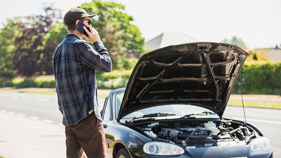 man on the phone while looking at car with open hood