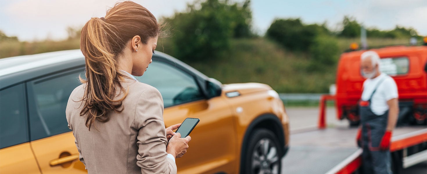 car going on tow truck next to woman on phone