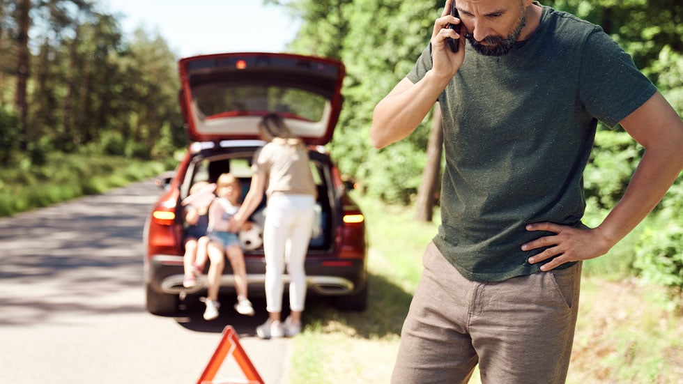 man on phone, car and family in the background, car troubles