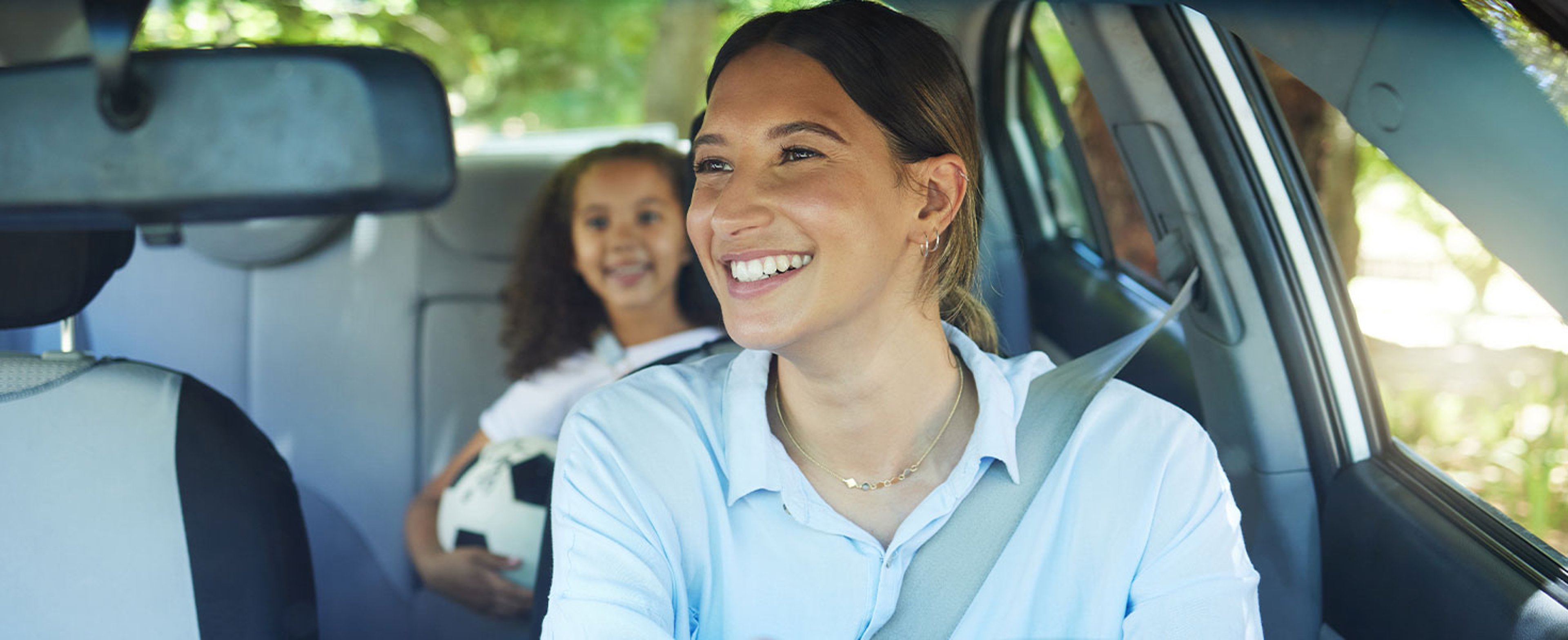 mom driving car, daughter in backseat holding soccer ball