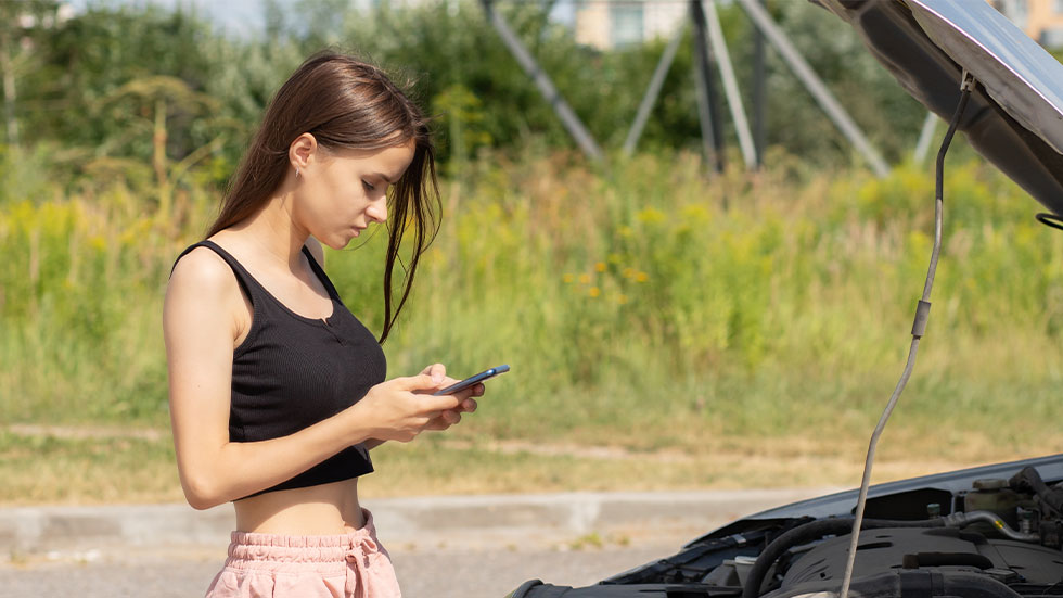 teenage girl standing by car with hood open while on cell phone