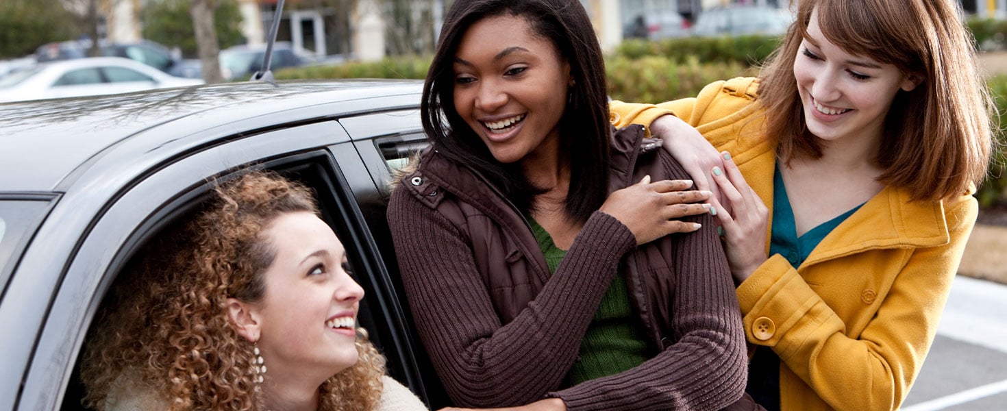teenage girl in car while talking to friends standing outside of car