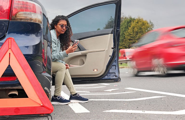 girl sitting in car with door open, traffic triangle in fram