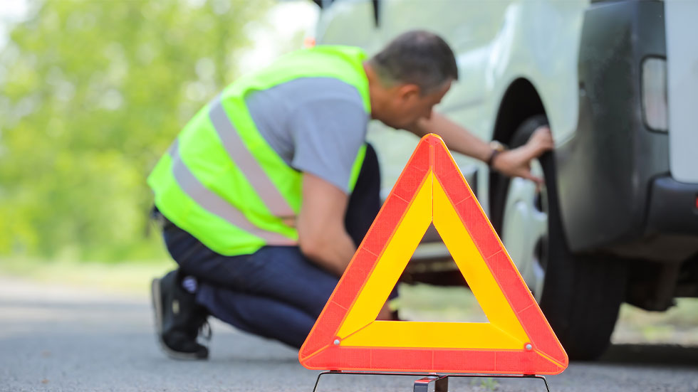 man changing car tire behind cation traffic triangle