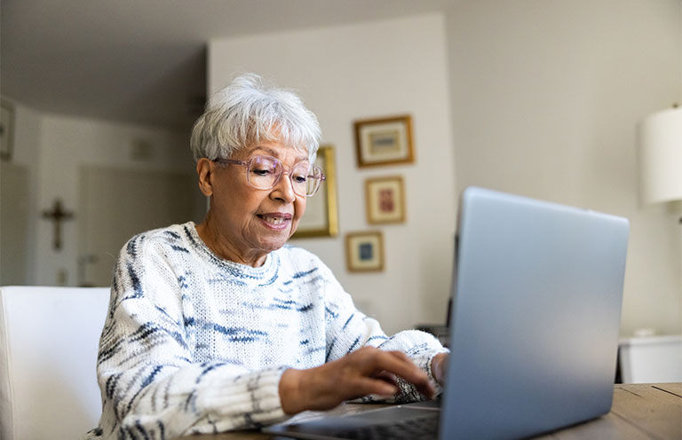 elder woman sitting at table using laptop