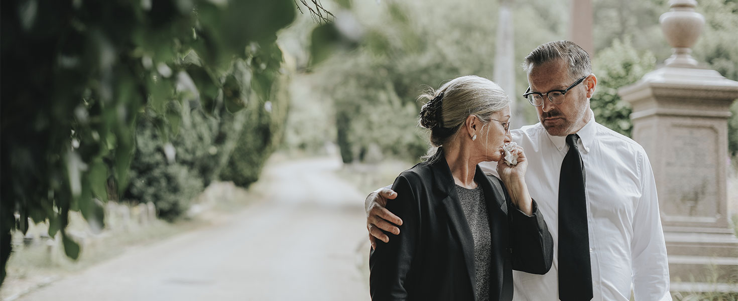 Two people walking through cemetary and supporting each other