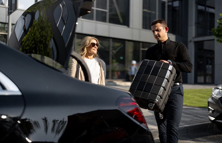 man putting woman's suitcase in car trunk