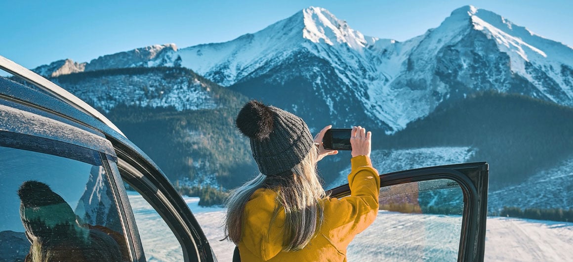 woman near car door, taking photo of mountains