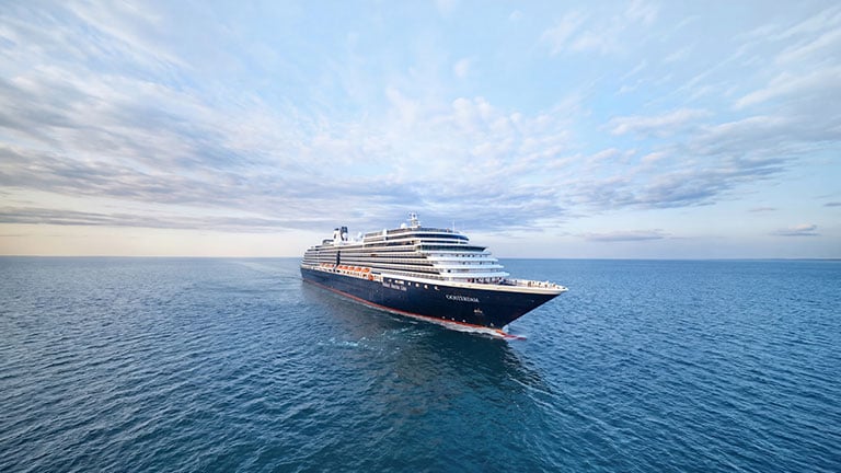 Holland America Line’s Oosterdam cruise ship sailing through calm waters with snowcapped mountains in the distance.