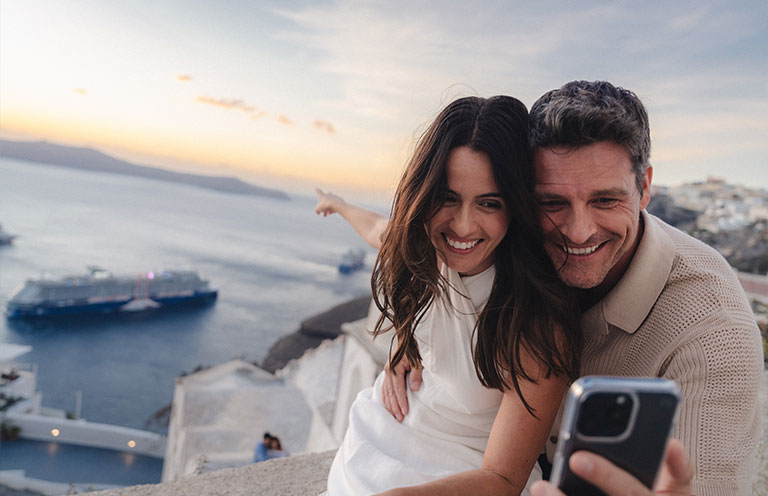 man and woman take selfie in Santorini Greece, Celebrity Cruise ship in the back