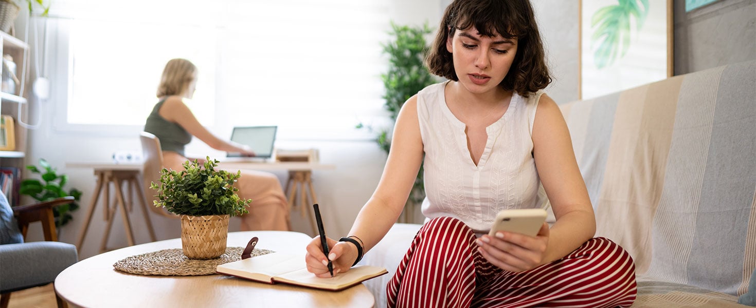 girl looking at phone and taking notes